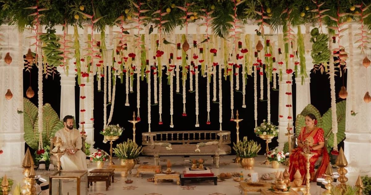 A bride and groom seated at a traditional ceremony under hanging garlands, marigolds and greenery