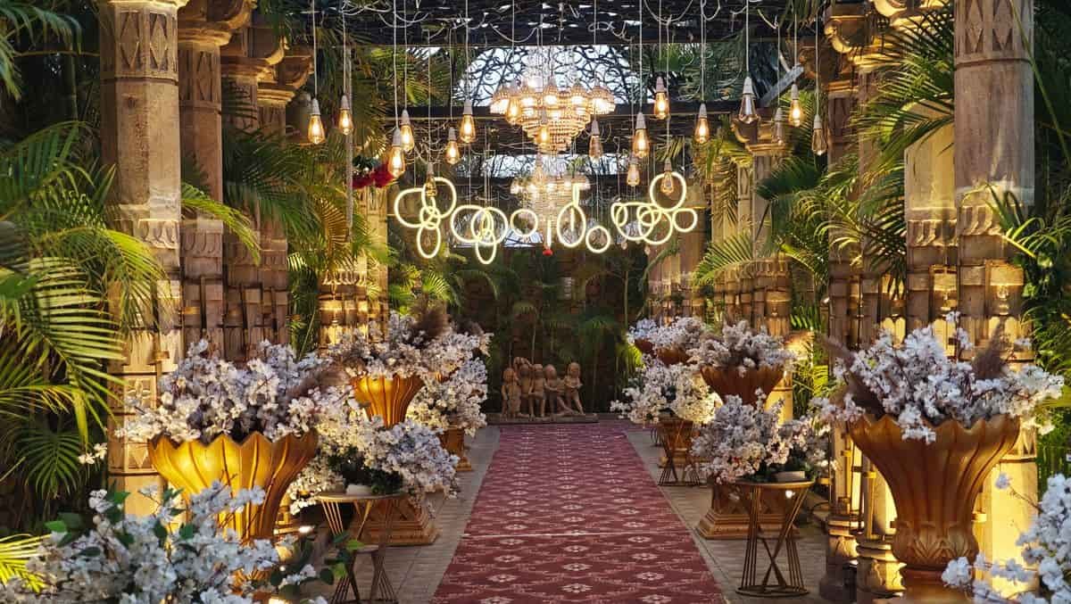 A garden entrance lit by hanging bulbs, glowing ring lights and a crystal chandelier above floral urns